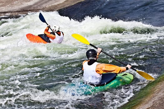 two active kayakers are rolling and surfing in rough water