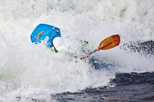 an active male kayaker rolling and surfing in rough water
