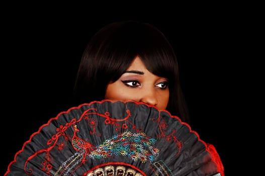 A head shoot of a pretty woman for black background, holding up a nice fan, covering her mouth.