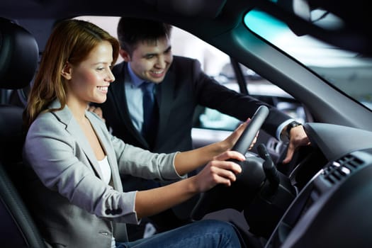 Photo of elegant woman sitting in car while listening to salesman in automobile center