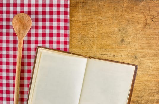 Wooden spoon and open book on a wooden board with checkered tablecloth