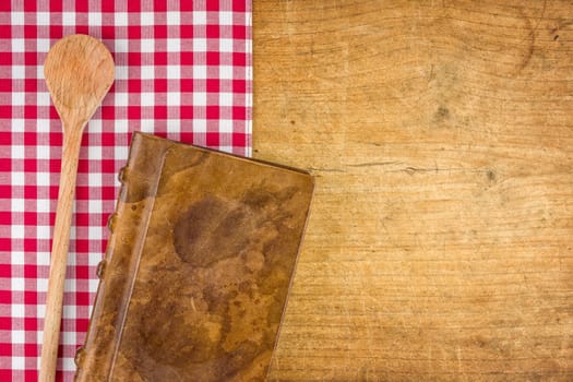 Wooden spoon and book on a wooden board with checkered tablecloth