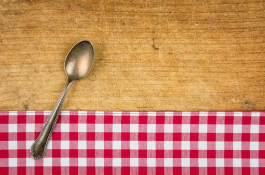 Silver spoon on a wooden board with checkered tablecloth