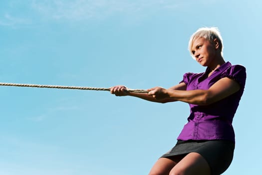 resolute business woman pulling rope against blue sky, symbol of power and determination. Copy space, side view