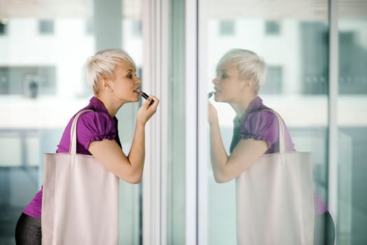 business woman in a hurry applying make up outdoor and looking at office building window