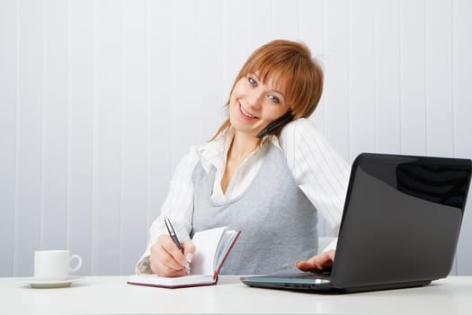 Attractive happy girl talking on the phone and writes simultaneously