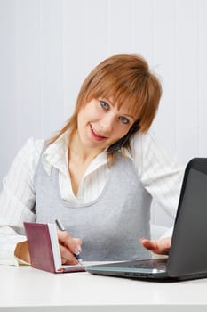 Attractive happy girl talking on the phone and writes simultaneously