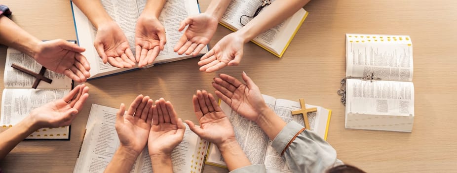 Cropped image of diversity people hand praying together at wooden church on bible book. Group of believer hold hand together faithfully. Concept of hope, religion, faith, god blessing. Burgeoning.