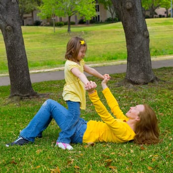Daughter and mother playing lying on park lawn outdoor dressed in yellow
