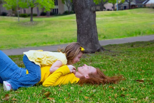 Daughter and mother playing lying on park lawn outdoor dressed in yellow