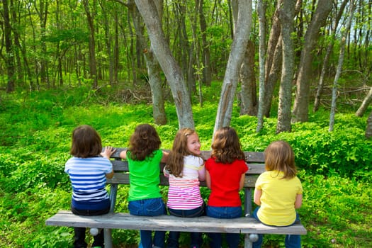 Children sister and friend girls sitting on park bench looking at forest and smiling