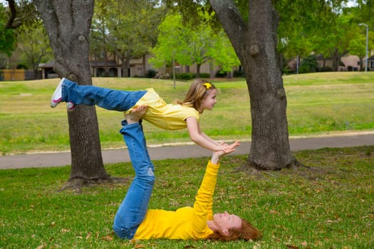 Daughter and mother playing keeping balance lying on park lawn outdoor