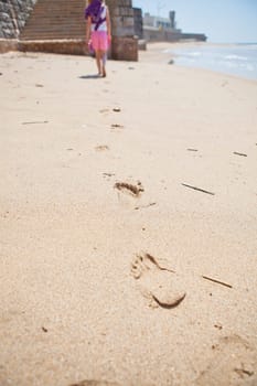 Young girl walking on beach at Areia Branca Portugal with footprints in foreground