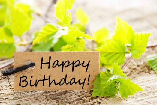 a natural looking label with happy birthday and green leaves and wood as background