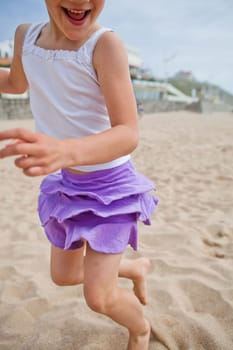 Closeup of happy barefoot young girl in purple skirt and white top playing on beach