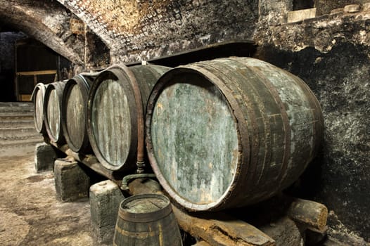 Five Old and Weathered Keg Barrels Stacked in Row Along Wall in Old Stone Wine Cellar