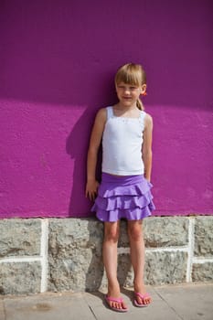 Portrait of cute young girl against purple painted concrete wall