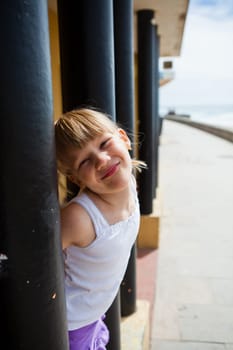 Smiling young girl between structural pillars alongside beachside walkway