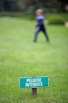 Details of a sign," keep off the grass""in a urban park, and a child is playing on it."