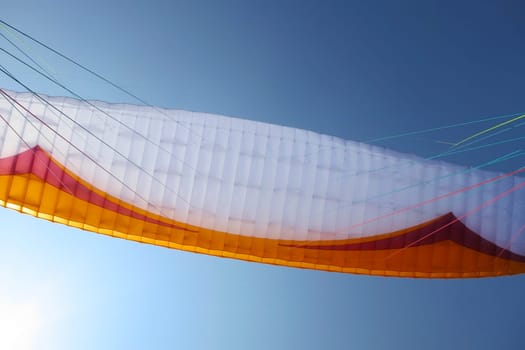 Paraglider wing in flight by a sunny day, blue sky background