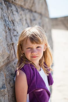 Closeup portrait of cute young girl leaning against brick wall at beach