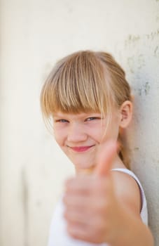 Closeup focus on face of cute smiling young girl doing thumbs up ok sign