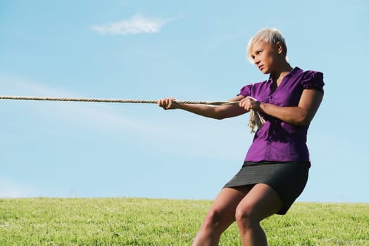 resolute business woman pulling rope against blue sky, symbol of power and determination. Copy space, side view