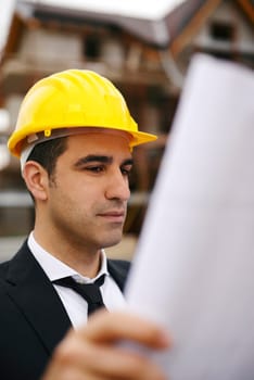 Young man working as engineer in new apartment buildings, looking at building plan in construction site