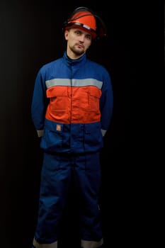 The worker in overalls and a helmet on a black background