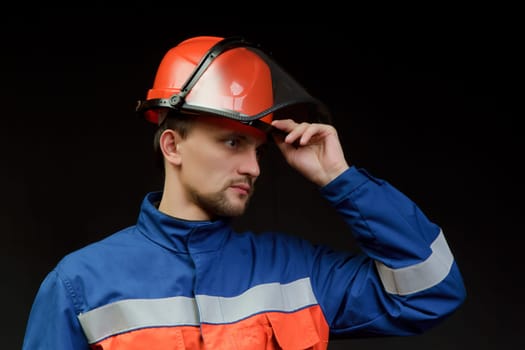 The worker in overalls and a helmet on a black background
