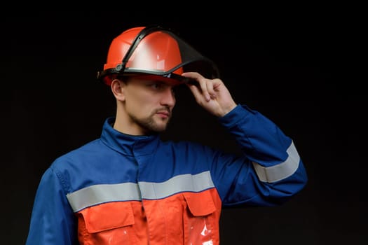 The worker in overalls and a helmet on a black background