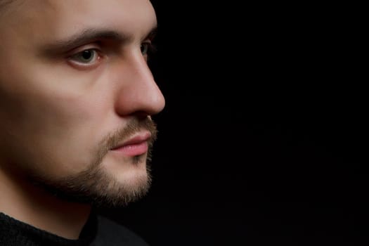 face of the young unshaven man in a black background