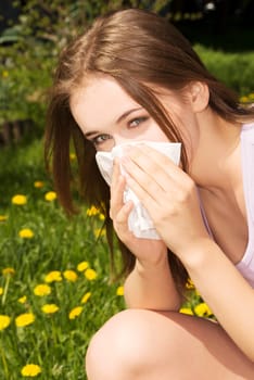 Young woman with allergy during sunny Day is wiping her nose.