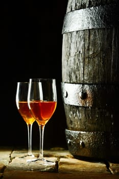 Old oak wine barrel with two glasses of sherry against a dark background reminiscent of a cellar in a winery
