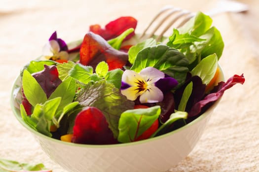Fresh herb salad with leafy greens and nasturtium flowers served in a white ceramic bowl