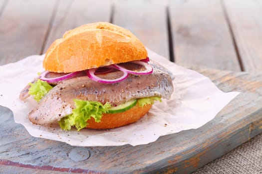 Seafood burger with a freshly baked crusty bun, fillet of fish, onion and lettuce served on a rustic wooden board