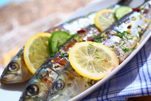 Close-up of three grilled sardines with lemons slices on a platter over a table outdoors