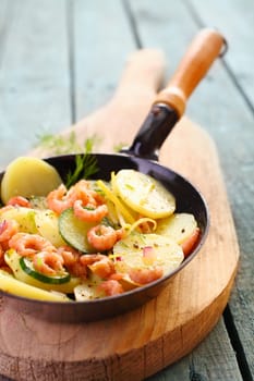 Prawns, zucchini and potato pan fried and served in the skillet on a wooden board for a healthy, fresh seafood meal