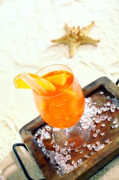 Daquiri and orange citrus cocktail standing on a wooden tray on a tropical beach with a starfish in the background