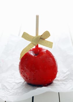 Festive colourful red toffee apple with a bow covered in hard sugary candy syrup for a holiday celebration