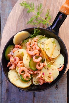 Delicious gourmet meal of prawns pan fried with potato and zucchini garnished with herbs and served in a metal skillet