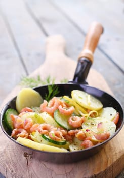 Pan fried shrimps and vegetables in a metal skillet with potato and zucchini garnished with herbs