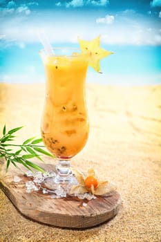 Elegant tall glass of delicious fruit cocktail on a tropical beach garnished with star anise standing on a wooden board