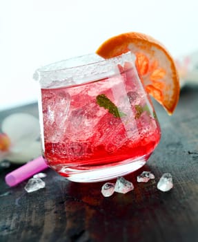 Ice cold daiquiri cocktail served in a tumbler garnished with orange on a wooden bar counter