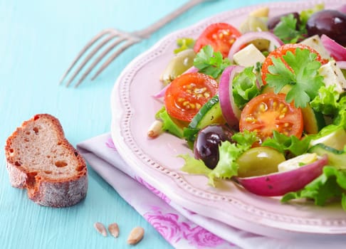 Rye bread and a plate of fresh feta salad with lettuce, olives, cherry tomato, onion rings and cucumber served on a white plate over a napkin