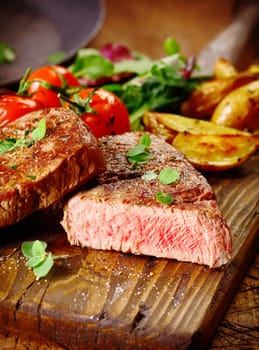 Portion of healthy lean grilled beef steak sliced through to reveal the rare interior served on a wooden board with roast vegetables