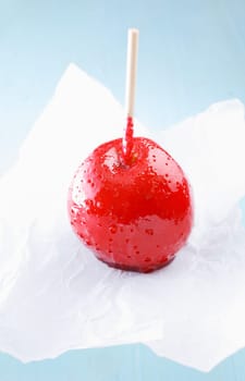 Delicious childhood candy or taffy apple coated in a colourful hard red sugar syrup standing on crumpled white paper