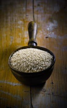 High-angle view of an old copper ladle filled with raw sesame over an old grungy golden wood table