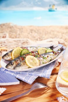 Whole garnished pan fried fish served at the beach on an oval platter garnished with lemon while enjoying a tropical summer vacation