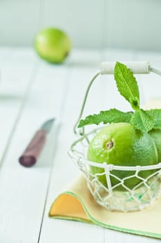 Fresh green limes in a country kitchen in a wire basket on white boards with a knife and copyspace